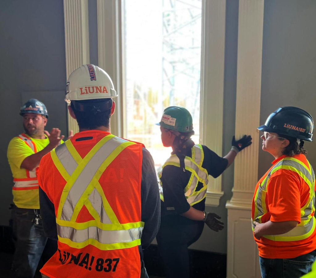 4 people in construction gear and hard hats in room talking