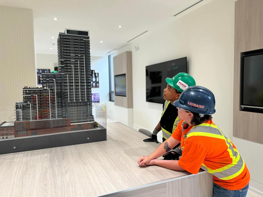 Two woman in construction headware and shirts looking at a miniature version of a business building