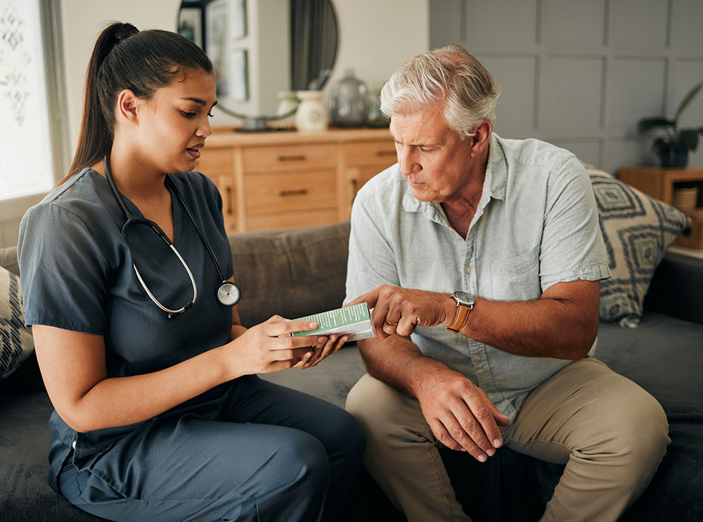 A nurse and an elderly man relax on a couch, illustrating a scene of compassion and connection in a home-like environment.