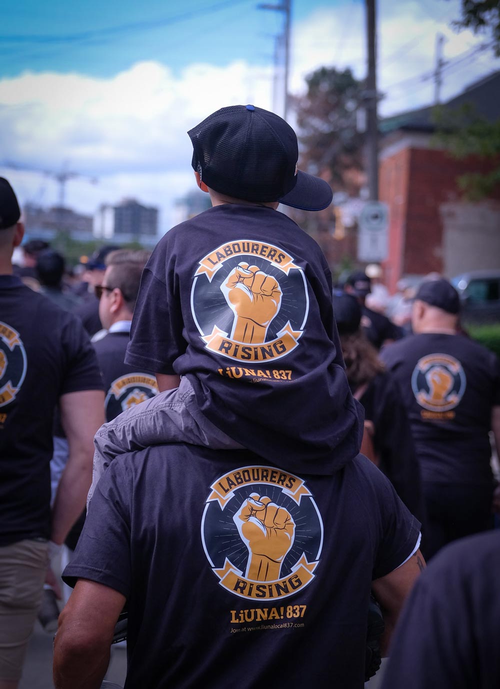 A boy with a baseball hat sitting on on the shoulders of a male both with t-shirts that showcase a fist in the air